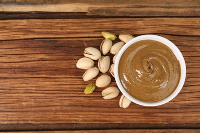 Photo of Delicious nut butter in bowl and pistachios on wooden table, top view. Space for text