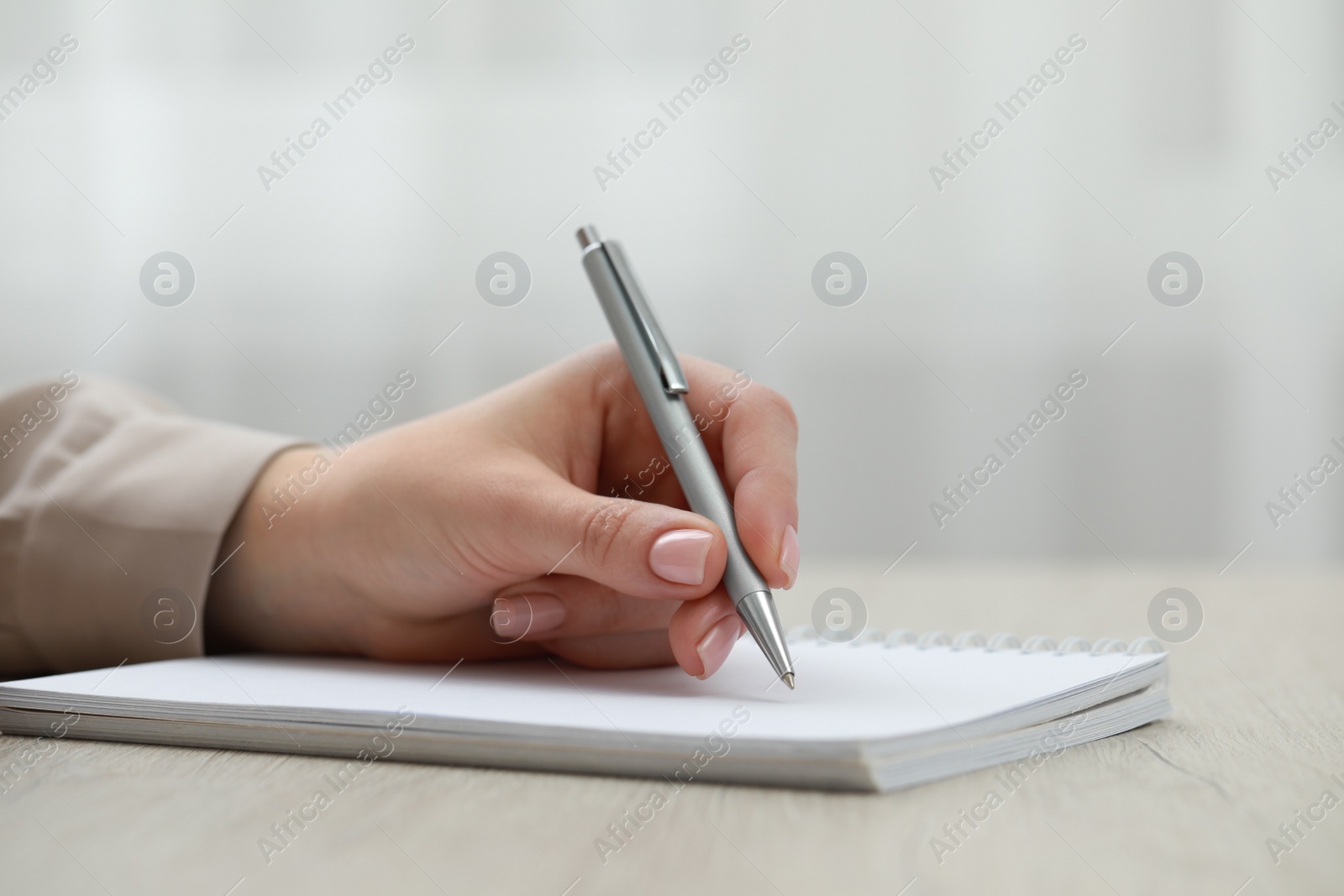 Photo of Woman writing in notebook at wooden table, closeup