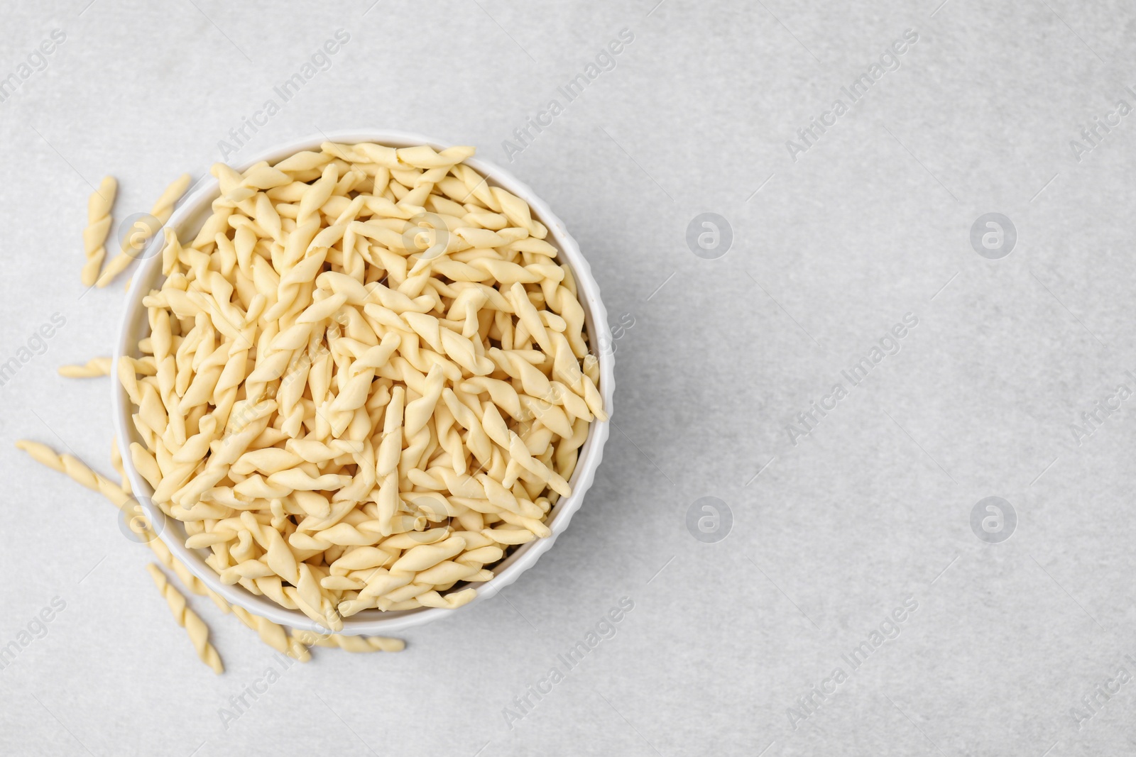 Photo of Bowl with uncooked trofie pasta on light grey table, flat lay. Space for text