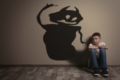 Image of Shadow of monster on wall and upset boy in room
