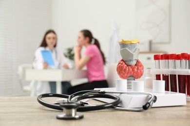 Photo of Endocrinologist examining patient at clinic, focus on stethoscope and model of thyroid gland