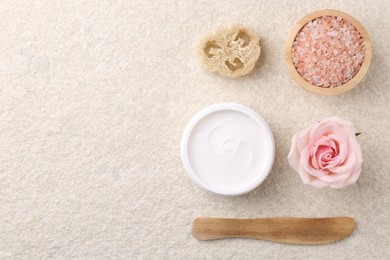 Flat lay composition with moisturizing cream in open jar and other body care products on light textured table. Space for text