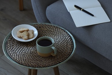 Photo of Cup of drink and cookies on coffee table near sofa indoors