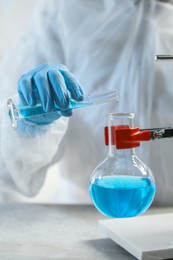 Scientist working with flask and test tube in laboratory, closeup