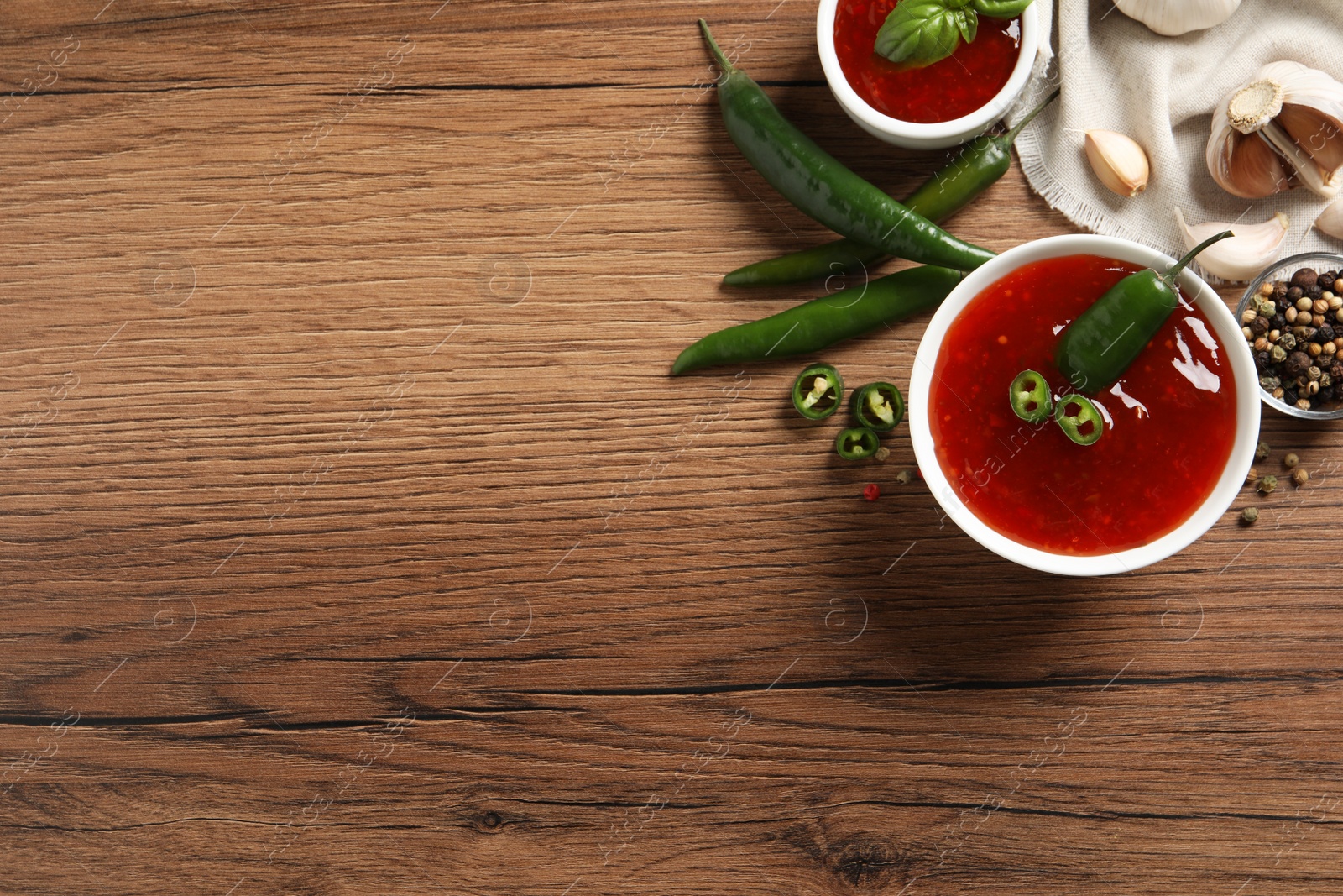 Photo of Spicy chili sauce and ingredients on wooden table, flat lay. Space for text