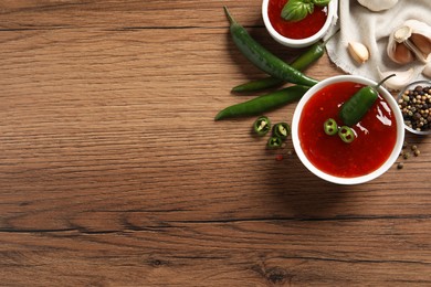 Photo of Spicy chili sauce and ingredients on wooden table, flat lay. Space for text