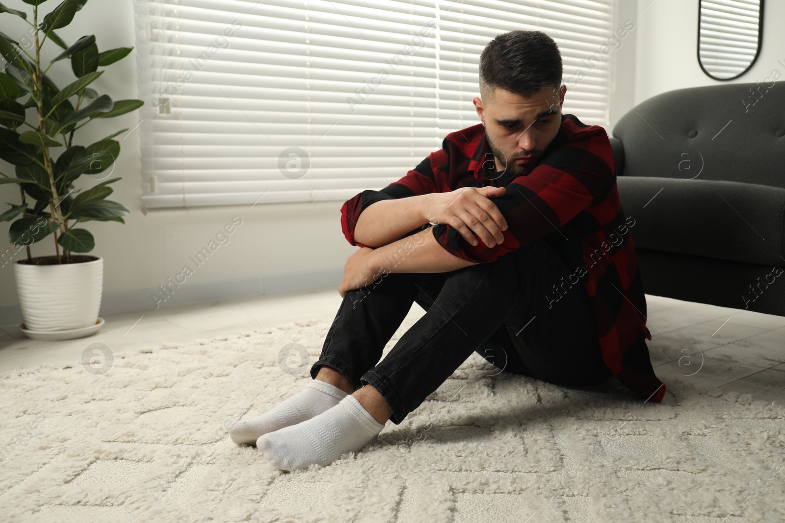 Photo of Sad man sitting on floor at home. Space for text