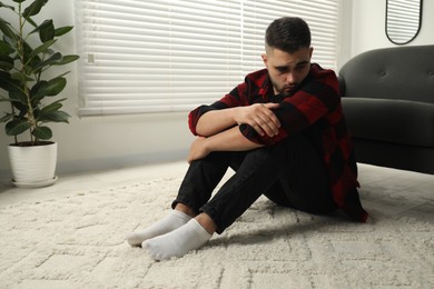 Photo of Sad man sitting on floor at home. Space for text