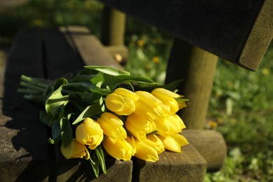 Photo of Bouquet of beautiful yellow tulips on wooden bench outdoors