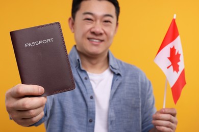Immigration. Happy man with passport and flag of Canada on orange background, selective focus