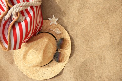 Stylish striped bag and beach accessories on sand, flat lay