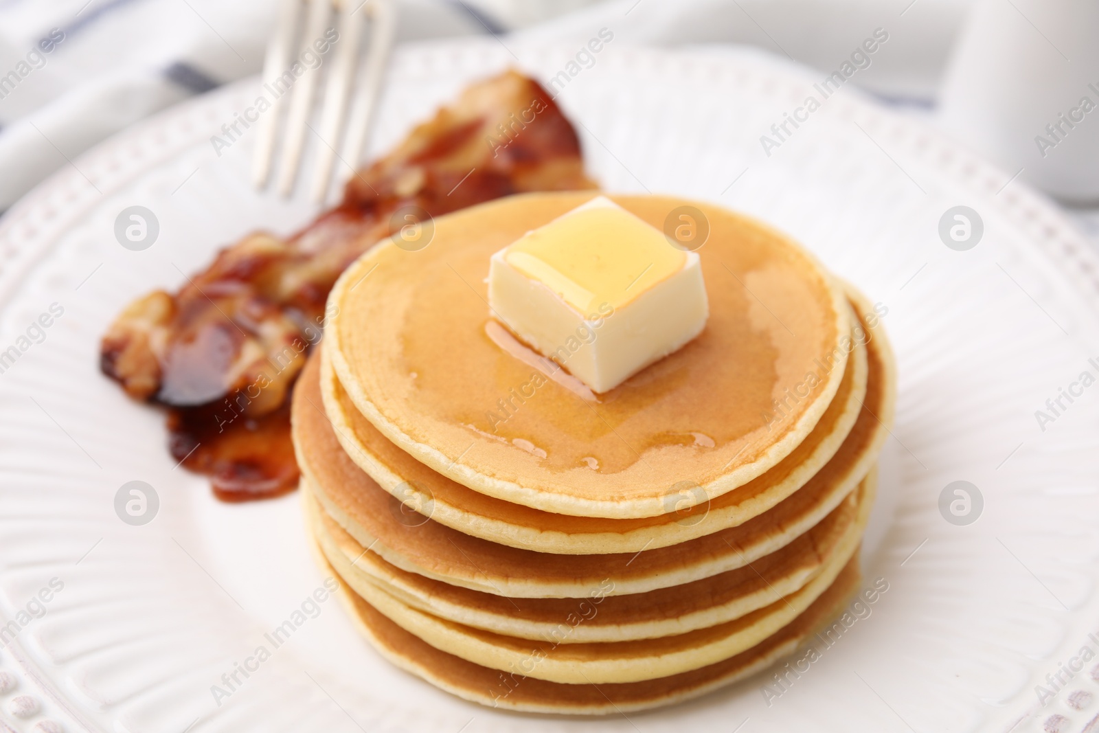 Photo of Delicious pancakes with butter, maple syrup and fried bacon on white marble table