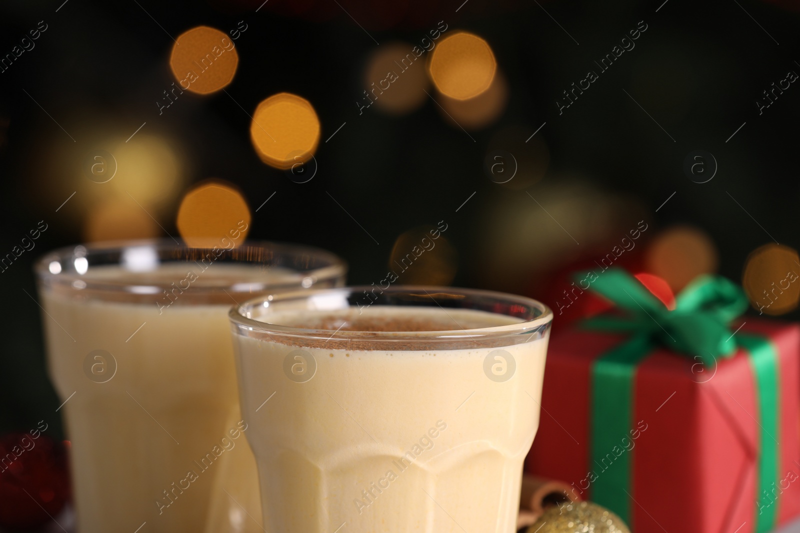 Photo of Tasty eggnog with cinnamon and gift box against blurred festive lights