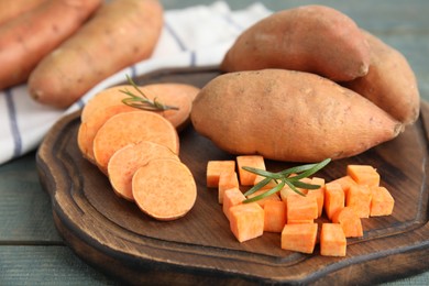 Wooden board with cut and whole sweet potatoes on table, closeup