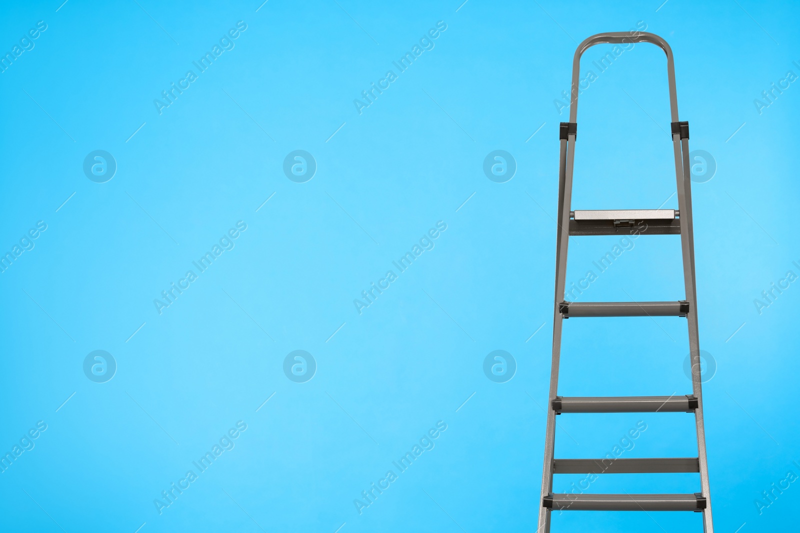 Photo of Metal stepladder on light blue background. Space for text