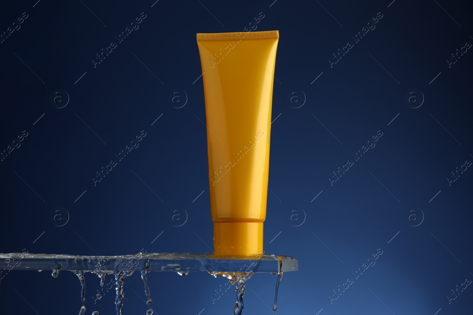 Photo of Moisturizing cream in tube on glass with water drops against blue background. Space for text