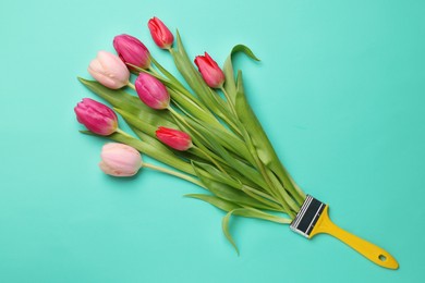 Photo of Brush with colorful tulips on turquoise background, top view. Creative concept