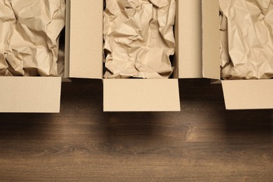 Photo of Open cardboard boxes with crumpled paper on wooden floor, flat lay and space for text. Packaging goods