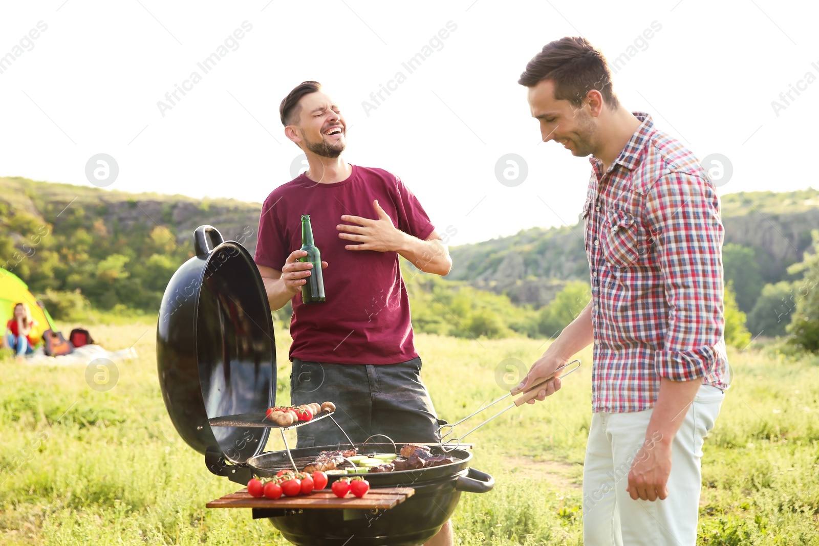 Photo of Young people having barbecue in wilderness. Camping season