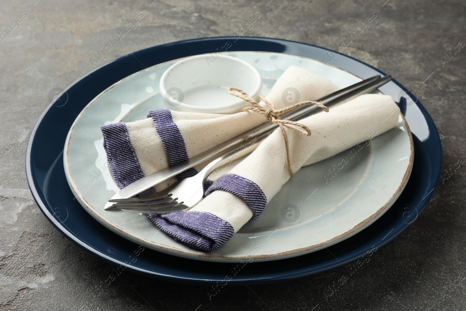 Photo of Stylish setting with cutlery, plates, bowl and napkin on grey textured table, closeup