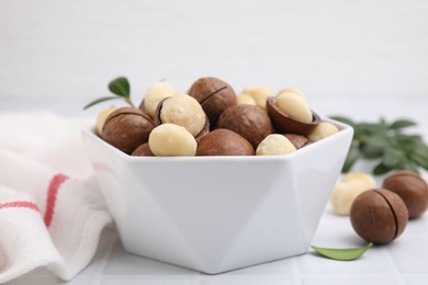 Tasty Macadamia nuts in bowl on white table, closeup