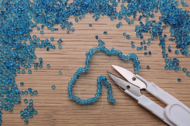 Photo of Bright light blue glass beads, bracelet and scissors on wooden table, flat lay