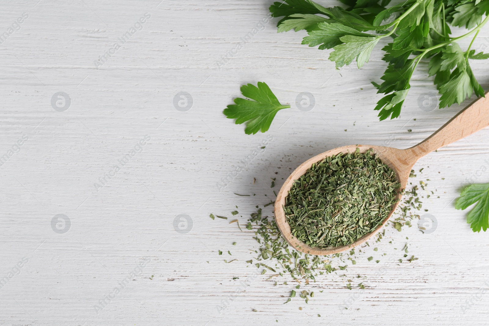 Photo of Spoon with dry parsley and space for text on white wooden background, top view