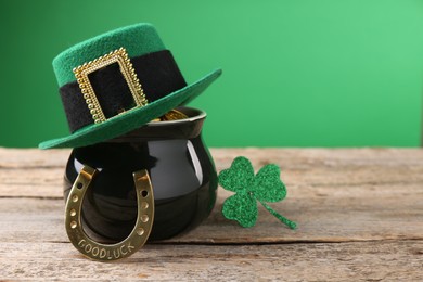 Photo of St. Patrick's day. Pot of gold with leprechaun hat, horseshoe and decorative clover leaf on wooden table. Space for text