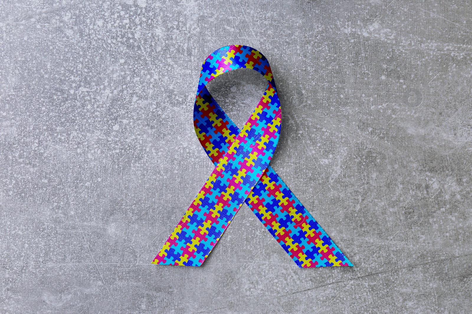 Image of World Autism Awareness Day. Colorful puzzle ribbon on light grey stone background, top view