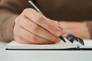 Photo of Man writing in notebook at white table, closeup