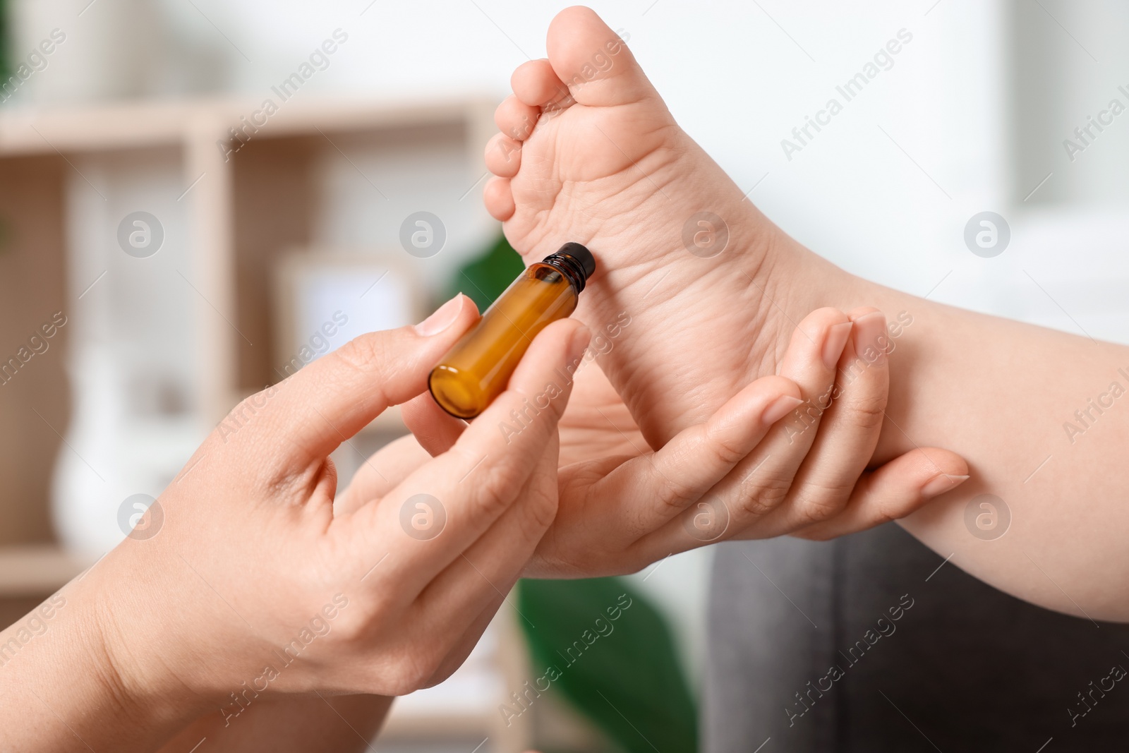 Photo of Mother applying essential oil from roller bottle onto her baby`s heel indoors, closeup