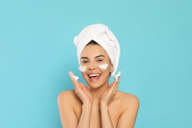 Photo of Happy young woman washing face with cosmetic product on light blue background