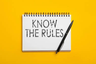 Image of Notebook with phrase Know the rules and pen on yellow background, top view