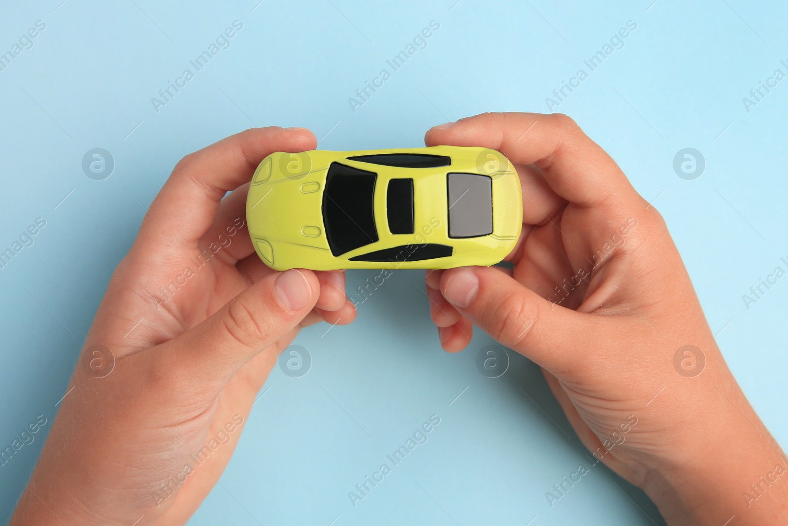 Photo of Child holding toy car on light blue background, top view