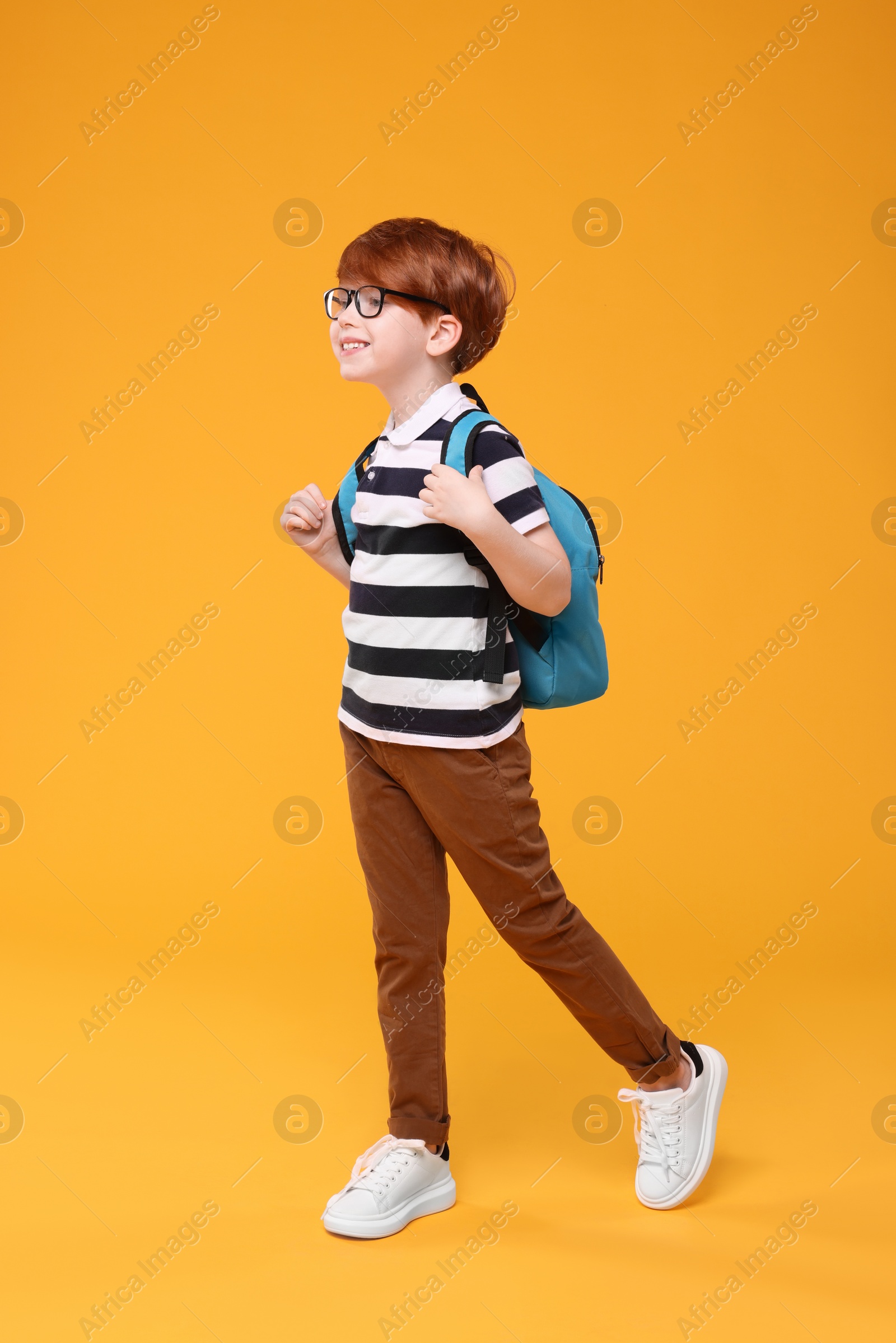 Photo of Happy schoolboy in glasses on orange background