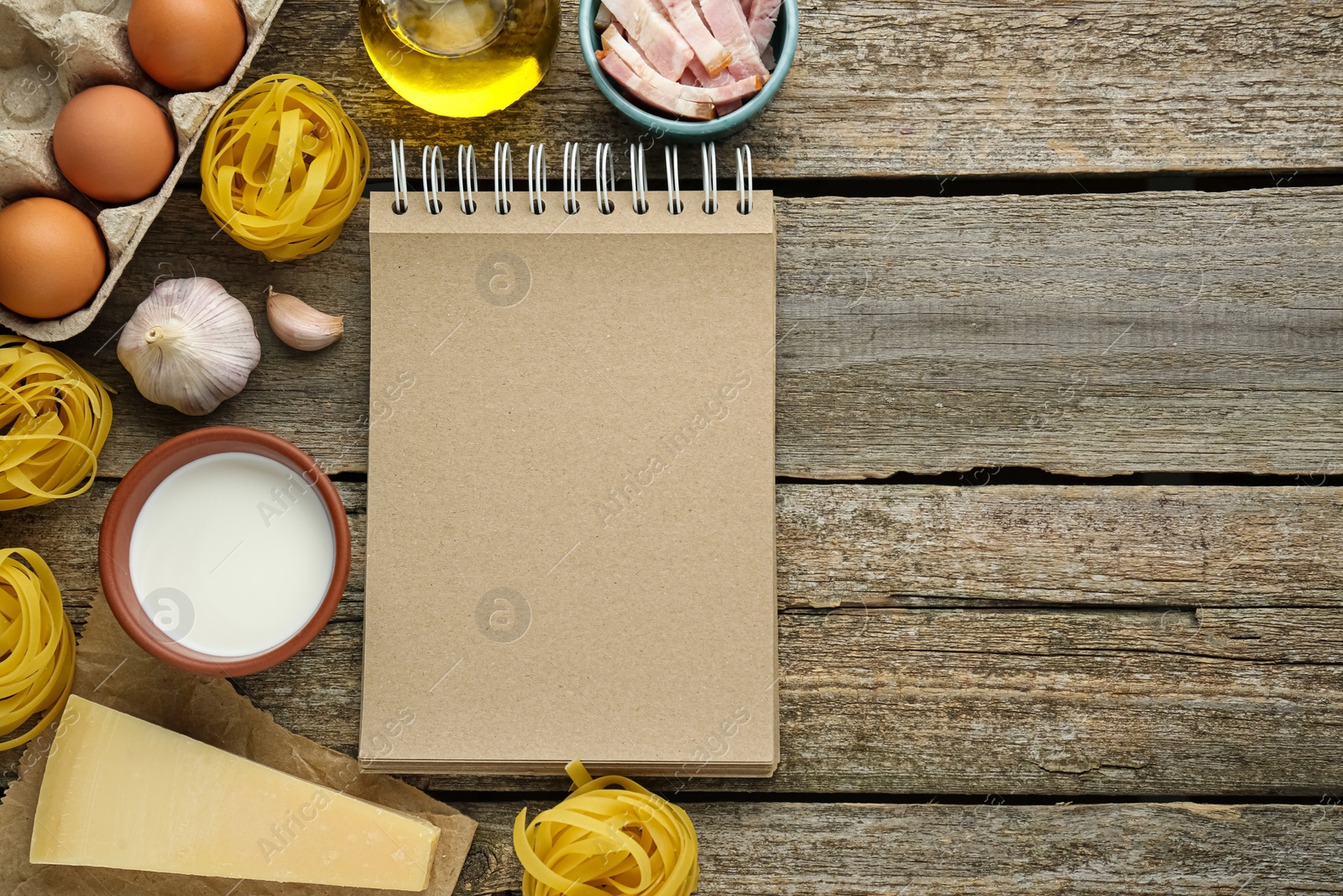 Photo of Blank recipe book and different ingredients on wooden table, flat lay. Space for text