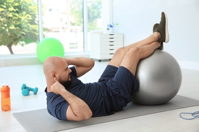 Overweight man doing exercise with fitness ball in gym