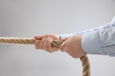Dispute concept. Man pulling rope on light grey background, closeup