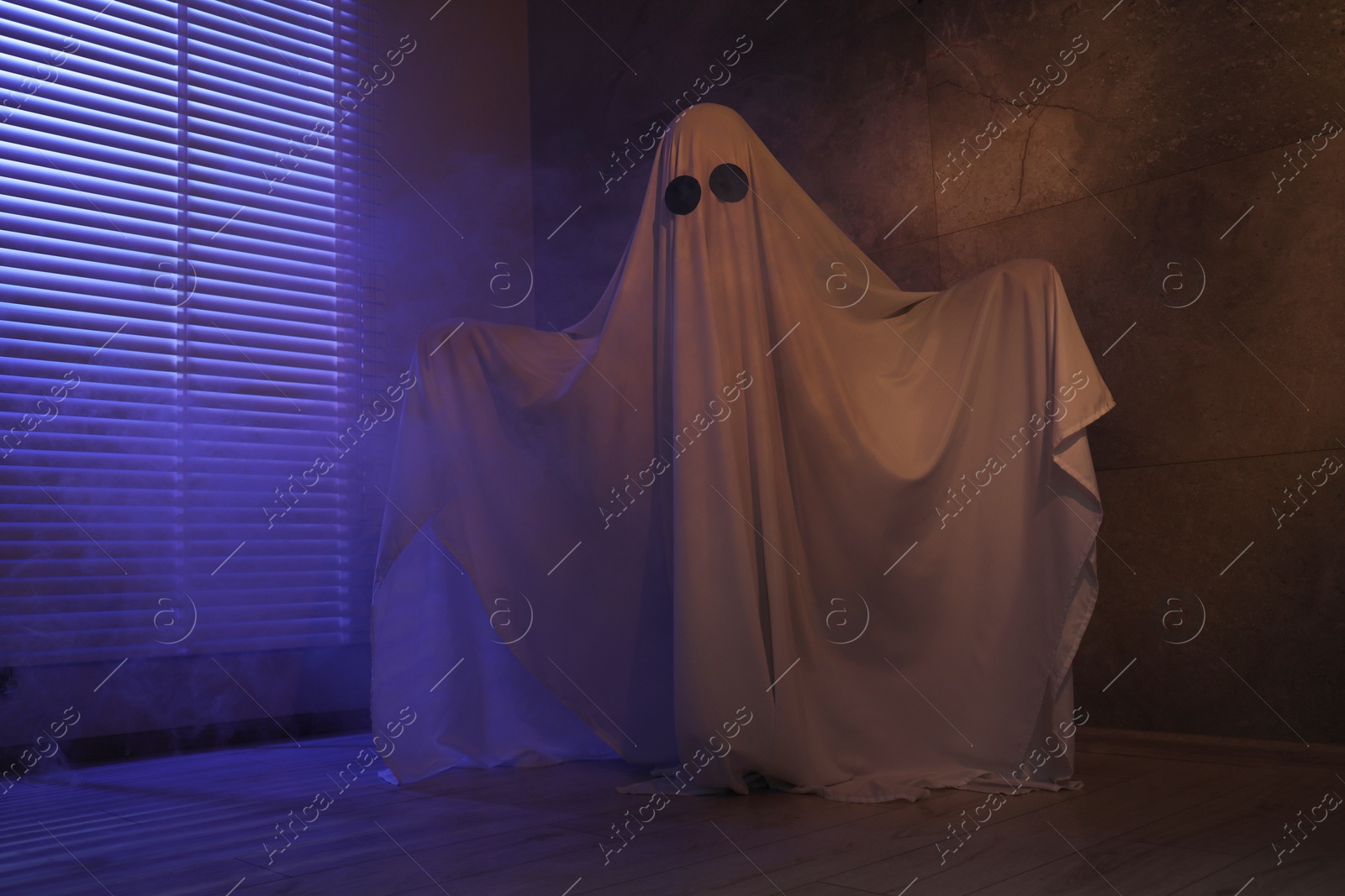 Photo of Creepy ghost. Woman covered with sheet near window in color lights