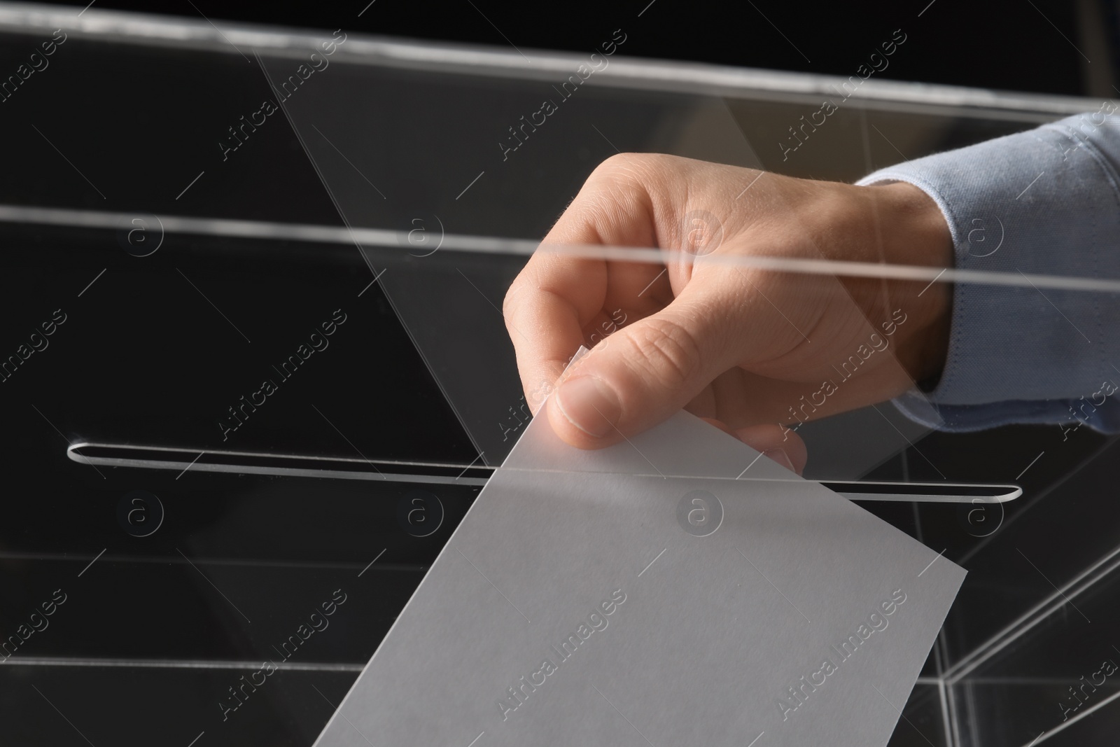 Photo of Man putting his vote into ballot box on black background, closeup