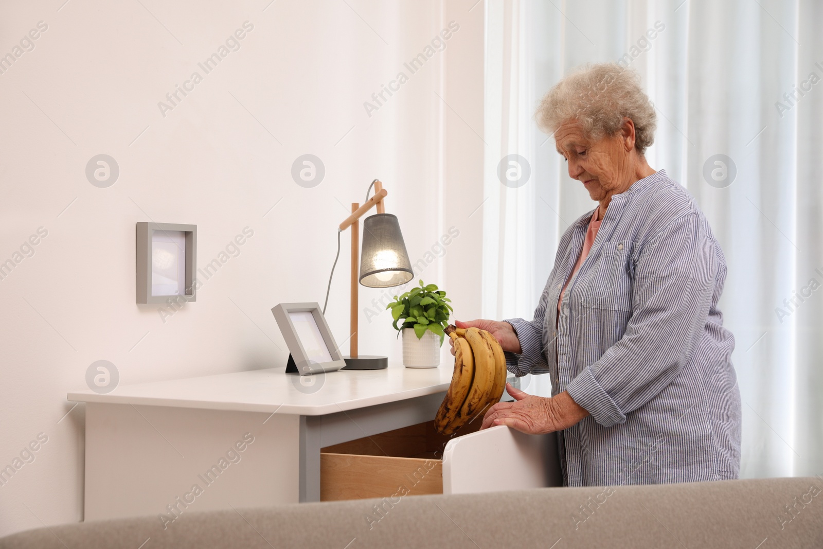 Photo of Senior woman finding bananas in chest of drawers at home. Age-related memory impairment