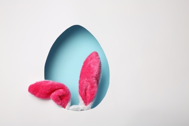 Photo of View of furry Easter bunny ears on color background through egg shaped hole, space for text