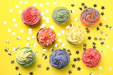 Photo of Delicious cupcake with bright cream and shiny confetti on yellow background, flat lay