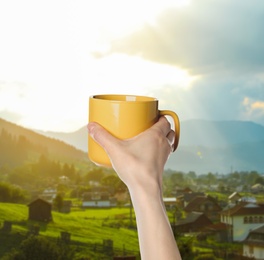 Image of Closeness to nature. Woman holding cup in mountain village, closeup