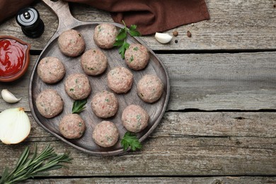 Photo of Many fresh raw meatballs and ingredients on wooden table, flat lay. Space for text