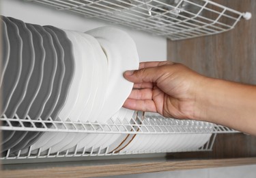 Photo of Woman taking ceramic plate from drying rack in kitchen, closeup