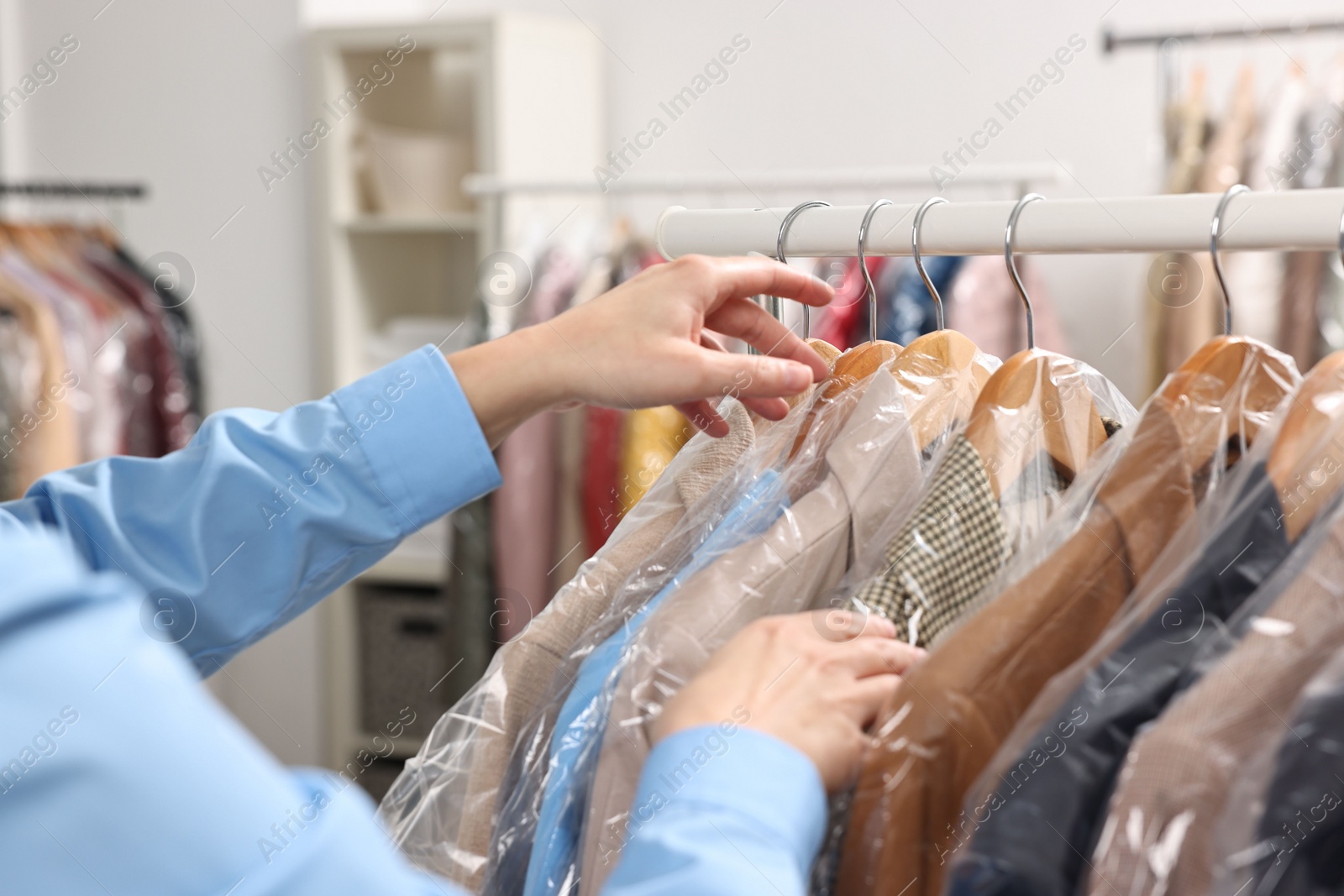 Photo of Dry-cleaning service. Woman taking jacket in plastic bag from rack indoors, closeup