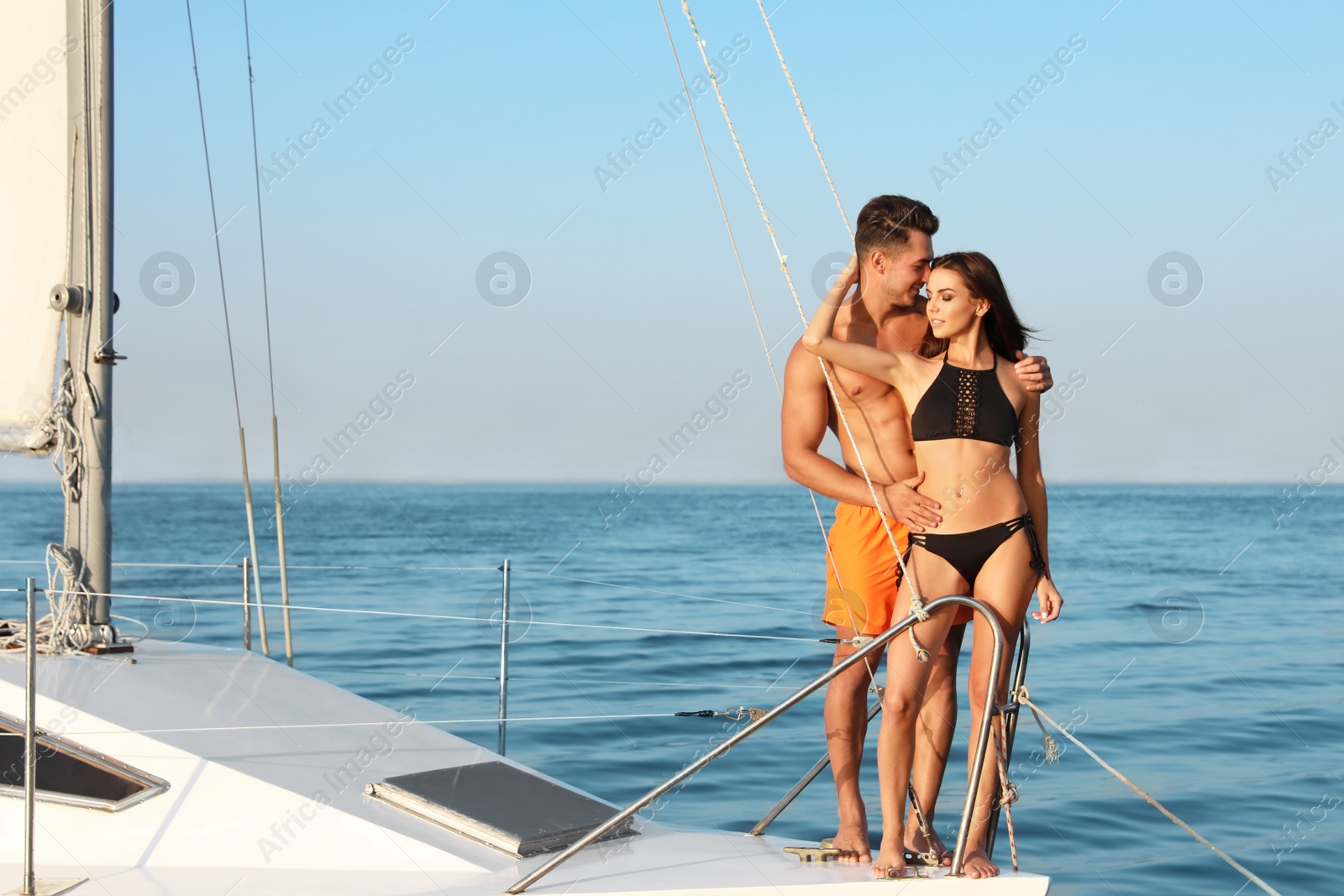 Photo of Young man and his beautiful girlfriend in bikini on yacht. Happy couple during sea trip