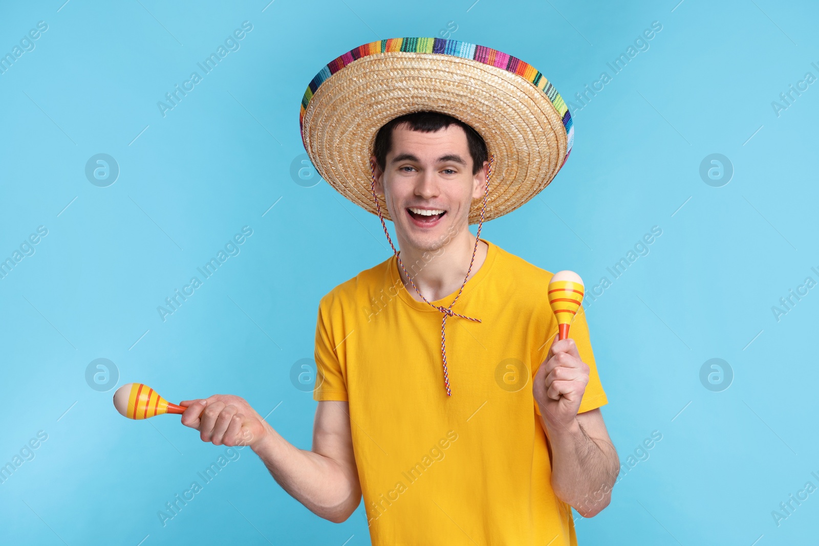 Photo of Young man in Mexican sombrero hat with maracas on light blue background