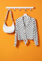 Photo of Hanger with polka dot shirt and bag on orange wall